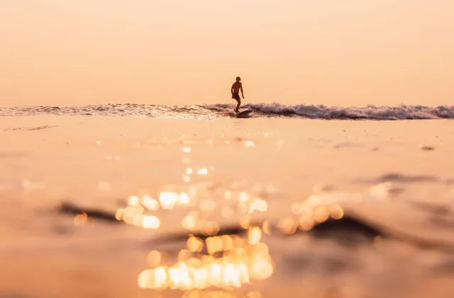 A surfer riding a small Atlantic wave at sunrise.